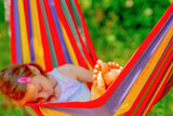 Fototapeta Natura - Young beautiful girl sleeping in a hammock with bare feet, relaxing and enjoying a lovely sunny summer day. Green vegetation in background. Happy childhood concept