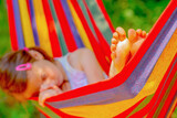 Fototapeta Natura - Young beautiful girl sleeping in a hammock with bare feet, relaxing and enjoying a lovely sunny summer day. Safety and happy childhood and leisure concept. Selective focus on bare feet