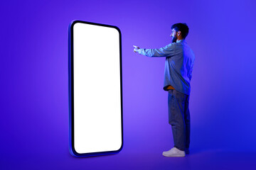 Wall Mural - guy stands scrolling on huge smartphone, neon blue studio backdrop