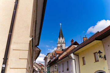 Wall Mural - Old town of Slovenian City of Kranj with colorful historic houses and church tower of Cerkev Svetega Kancijana church on a sunny day. Photo taken August 10th, 2023, Kranj, Slovenia.