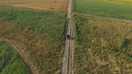 Wall Mural - Agricultural tractor with empty wagon trailer on countryside dirt road in summer, casting shadow on the ground, aerial shot from drone pov