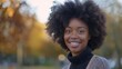 Close-up portrait of an attractive young African American woman wearing warm knitted sweater posing outdoors. Cheerful smiling black female model in autumn park.