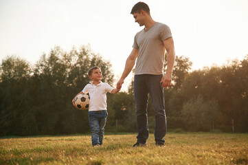 Wall Mural - Walking and holding soccer ball. Father and little son are playing and having fun outdoors