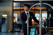 © Drazen - Happy hotel attendant pushing luggage cart through the hallway.
