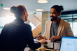 © Drazen - Happy African American man talking to hotel receptionist while filing registration paperwork at front desk.