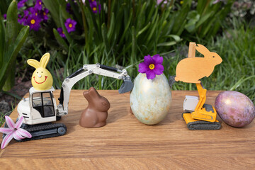 two models of toy excavators, Easter eggs, rabbits on a background of spring plants. Easter holiday concept for construction companies. postcard for business