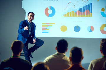 Professional giving talk on data science with detailed analytical visualization projected behind him at meeting room. Concept of business, startup, leadership and personal development courses.