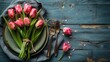 Cutlery and spring tulips set this Easter table. The background is made from wood with holidays on it.