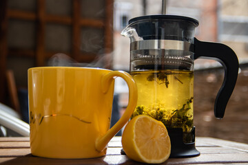 Wall Mural - Teapot (French press) with half lemon and teapot at wooden table on the balcony, morning tea time, aromatic aromatherapy fresh and herbal, organic tea from farm. In background neighborhood buildings