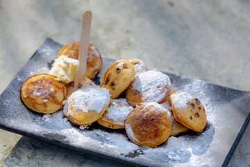 Selective focus of poffertjes on marble table, Traditional Dutch batter treat with white icing sugar on top, Resembling small fluffy pancakes they are made with yeast and buckwheat flour, Netherlands.