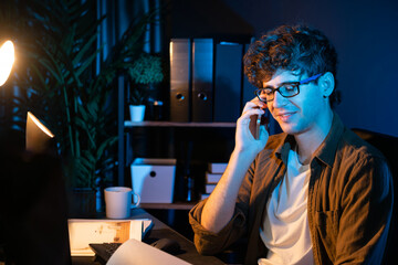 Young businessman calling on smartphone to customer or coworker, looking at computer screen of creative presentation surround work desk at neon modern office. Concept of new next project. Gusher.