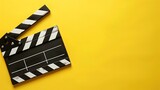 Fototapeta  - Na jasnożółtym tle znajduje się stary klaps filmowy w klasycznym czarno-białym designie, symbolizujący rozpoczęcie lub zakończenie nagrywania na planie filmowym.