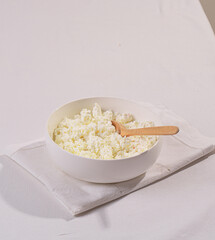 Wall Mural - Homemade crumbly cottage cheese in a white bowl on a white table