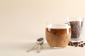 Wall Mural - Refreshing iced coffee with milk in glass, beans and spoons on beige background, space for text