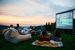 Group of friends relaxing while watching movie on patio at sunset.
