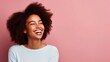 Close up portrait of a beautiful carefree young african american woman with an afro hairstyle laughing with her eyes closed on an isolated pink background with copy space