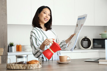 Poster - Beautiful young Asian woman pouring espresso from geyser coffee maker into cup and reading newspaper in kitchen