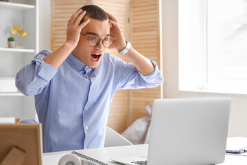 Wall Mural - Afraid young businessman with laptop sitting at table in office