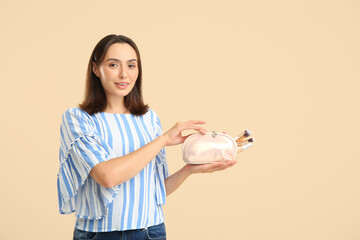 Wall Mural - Beautiful young woman with cosmetic bag full of makeup products on beige background