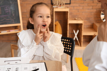 Wall Mural - Cute little girl with speech therapist pronouncing letters at table in office