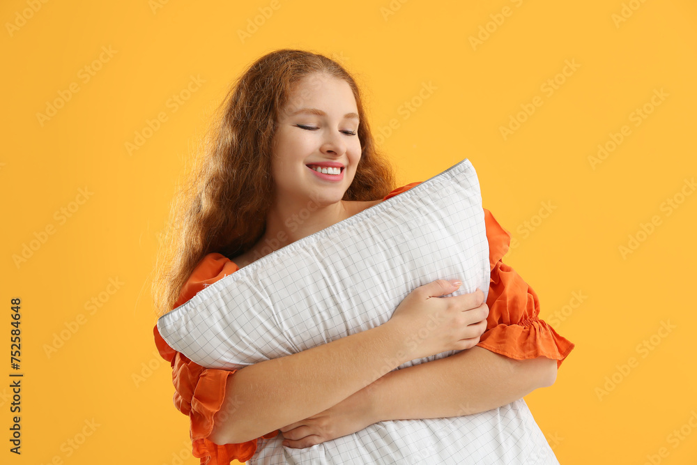 Beautiful young woman with white soft pillow on orange background