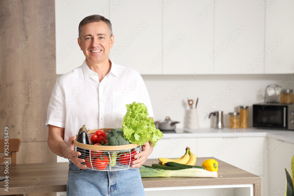 Mature man with basket of fresh vegetables in kitchen