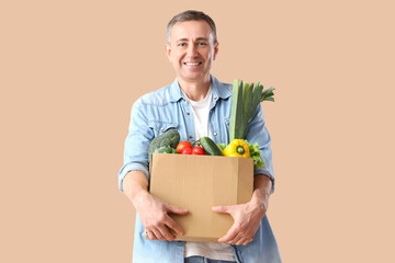 Canvas Print - Mature man with box of fresh vegetables on beige background