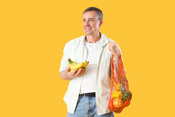 Wall Mural - Mature man with string bag of healthy food on yellow background