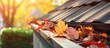 A metal gutter on a red brick residential roof is completely clogged with leaves and debris, potentially causing drainage issues and water damage. The overflowing leaves are a common sight in