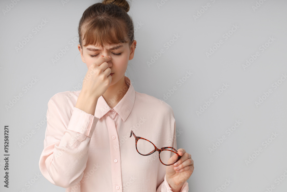 Tired young businesswoman with eyeglasses on light background. Glaucoma awareness month