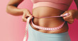 A woman in workout attire is measuring her waist with a pink measuring tape against a pink background.