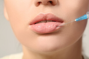 Poster - Young woman receiving lip injection against grey background, closeup