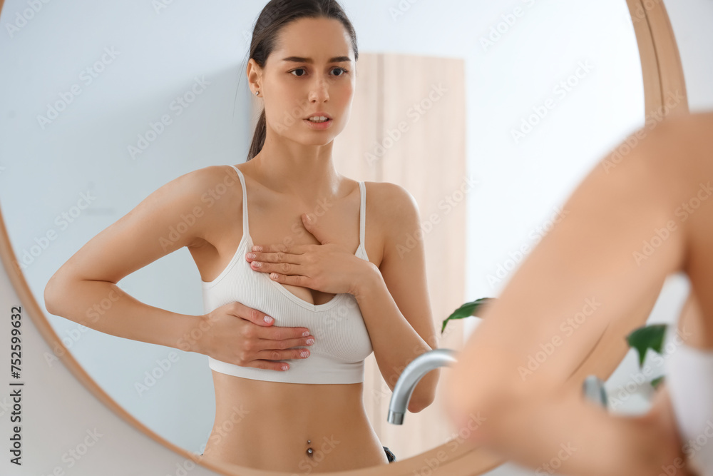 Young woman checking her breast near mirror in bathroom. Cancer awareness concept