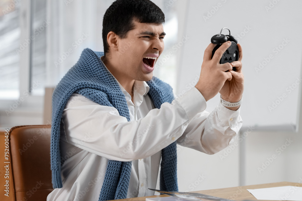 Stressed young businessman with alarm clock in office