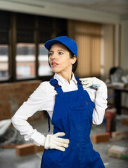 Wall Mural - Positive young woman repairer in uniform standing inside apartment and looking at camera