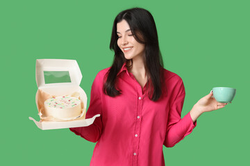 Poster - Beautiful young woman holding box with sweet bento cake and cup of coffee on green background. International Women's Day