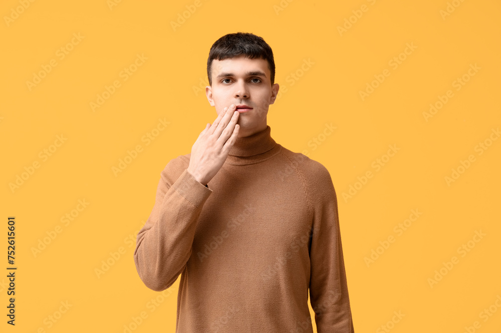 Young deaf mute man using sign language on yellow background