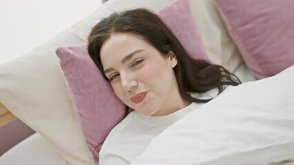 Sticker - A young caucasian woman relaxes in a cozy bedroom with white and purple bedding, conveying comfort and leisure