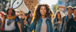 © NPix - Young African American activist leading a protest march holding a megaphone. Generative AI.