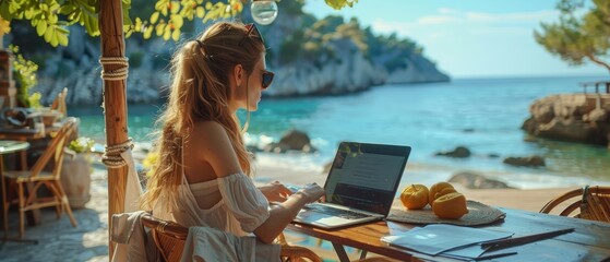 A woman enjoys the ultimate freedom of a digital nomad's life, working on a laptop at a beach cafe with a serene sea view.