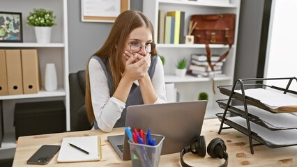 Wall Mural - Young blonde businesswoman shocked, covers mouth with hands amid mistake, secret worries evident in office