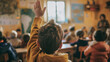 child in his classroom in the foreground raising his hand to ask his teacher a question