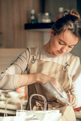 Wall Mural - woman bakery shop owner pours confetti into a bag for customer order. Bakery chef baking pastry and cake in kitchen. Small business entrepreneur and food delivery concept.