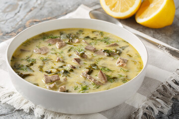 Greek Easter soup with lamb offal, herbs, seasoned with egg and lemon sauce close-up in a bowl on a marble table. Horizontal