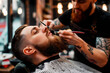 Tattooed barber meticulously styles a man's beard creating a modern look in modern barbeshop