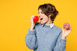 © ViDi Studio - Young excited Caucasian woman she wearing grey knitted sweater shirt casual clothes holding in hand sweet donut biting eat apple isolated on plain yellow background studio portrait. Lifestyle concept.