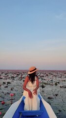 Wall Mural - happy woman in a white dress and hat is leisurely sitting in a boat on calm waters, with the sky and horizon in the background, enjoying the peaceful landscape and gentle wind Red Lotus sea, Thailand