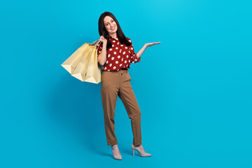 Sticker - Full size photo of good mood person wear red blouse hold clothes on shoulder palm show offer empty space isolated on blue color background