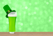 Glass Of Green Beer With Green Top Hat On Green Blurred Background. Saint Patrick's Day Concept. Empty Space For Text