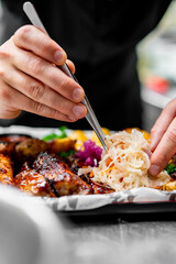 Poster - close-up view of hands garnishing grilled meat on a plate. The hands, holding tweezers, meticulously place an item onto the dish. The glossy surface of the grilled meat suggests it might be glazed